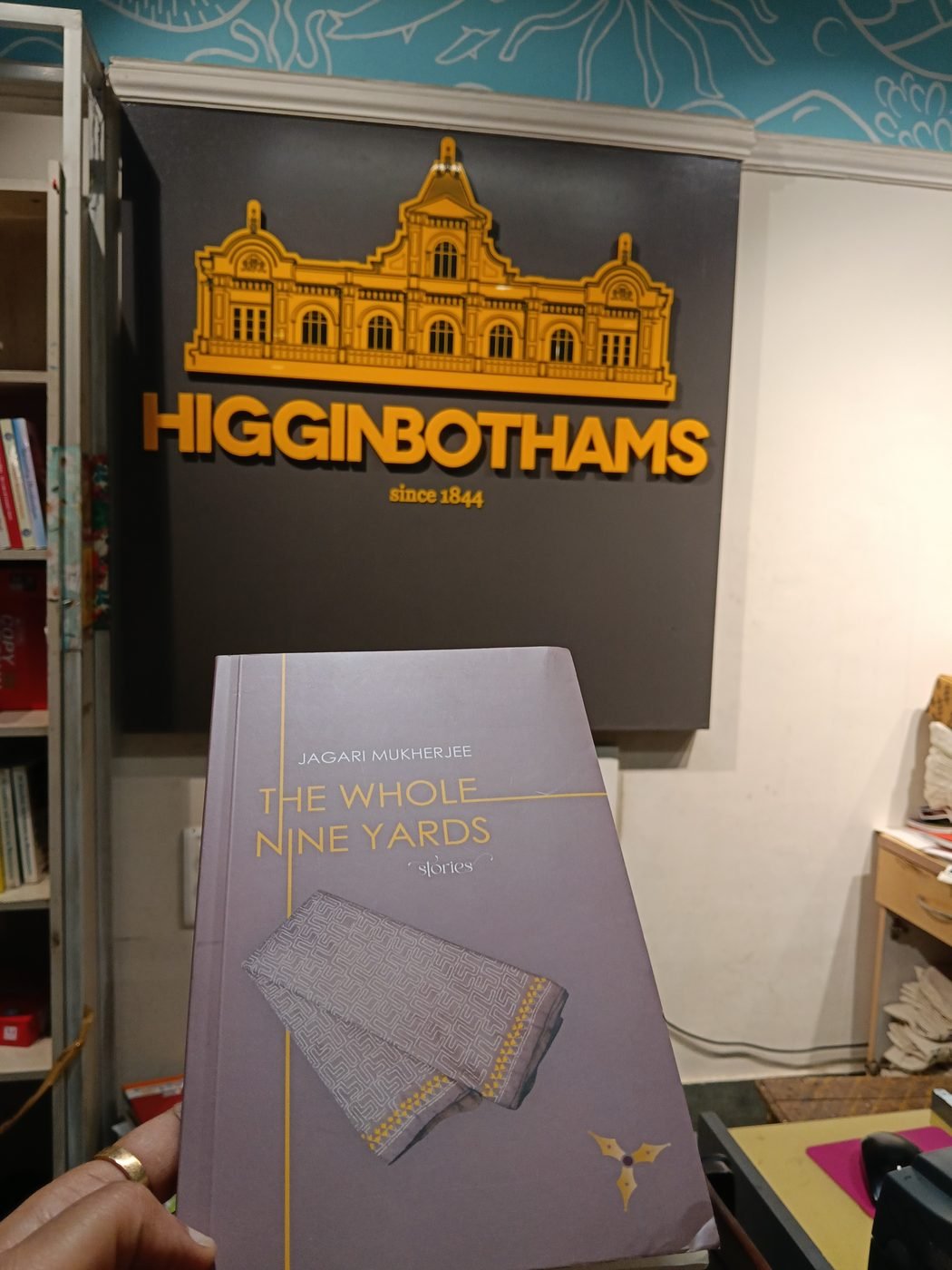 The Whole Nine Yards by Jagari Mukherjee held up in front of the Higginbothams sign